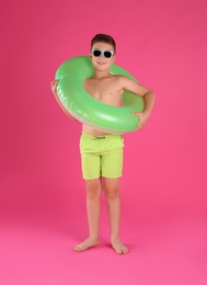 Cute little child in beachwear with bright inflatable ring on pink background