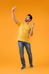 Photo of Emotional man taking selfie with smartphone on yellow background