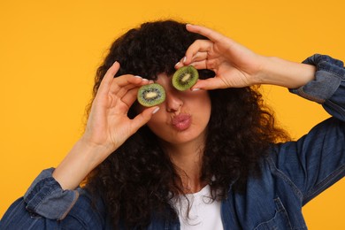 Photo of Woman covering eyes with halves of kiwi on yellow background