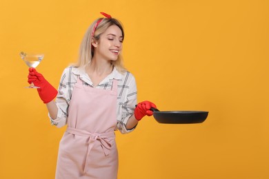 Photo of Young housewife with frying pan and glass of martini on yellow background. Space for text