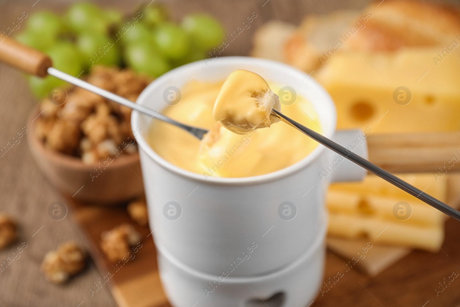 Photo of Pot of tasty cheese fondue and forks with bread pieces on wooden table