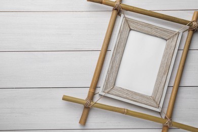 Photo of Empty bamboo frame on white wooden table, top view. Space for text