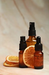 Photo of Bottles of organic cosmetic products and dried orange slices on marbled background