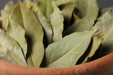 Photo of Aromatic bay leaves with wooden bowl as background, closeup view