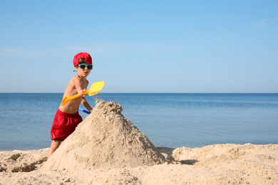Photo of Cute little child playing with plastic shovel at sandy beach on sunny day