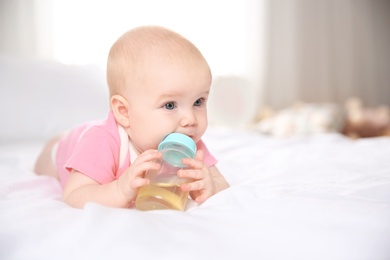Photo of Pretty baby lying with bottle on bed at home. Space for text