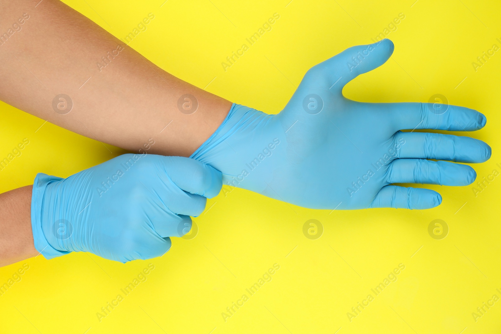 Photo of Person putting on blue latex gloves against yellow background, closeup