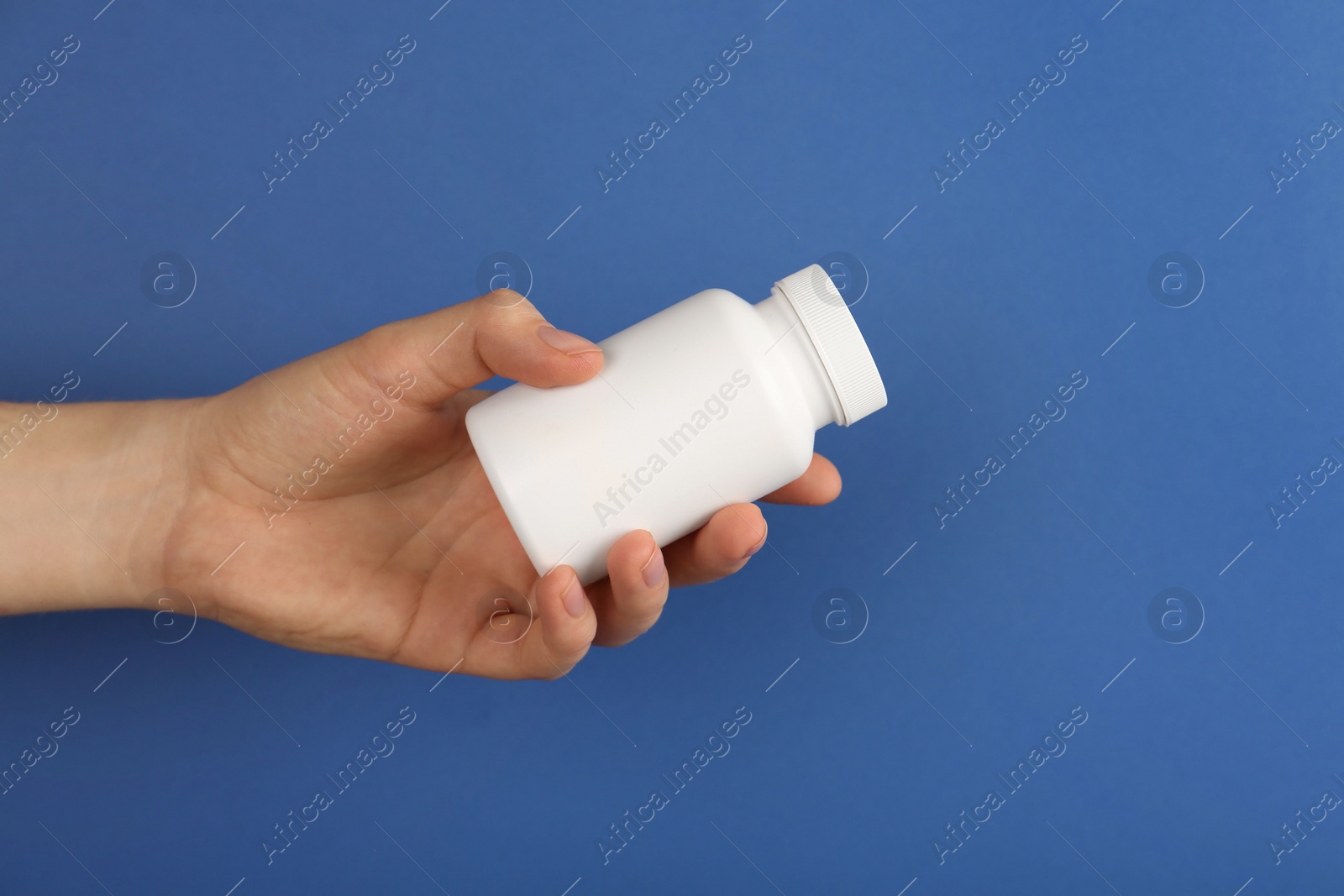 Photo of Woman holding blank white jar of vitamins on blue background, closeup. Space for text