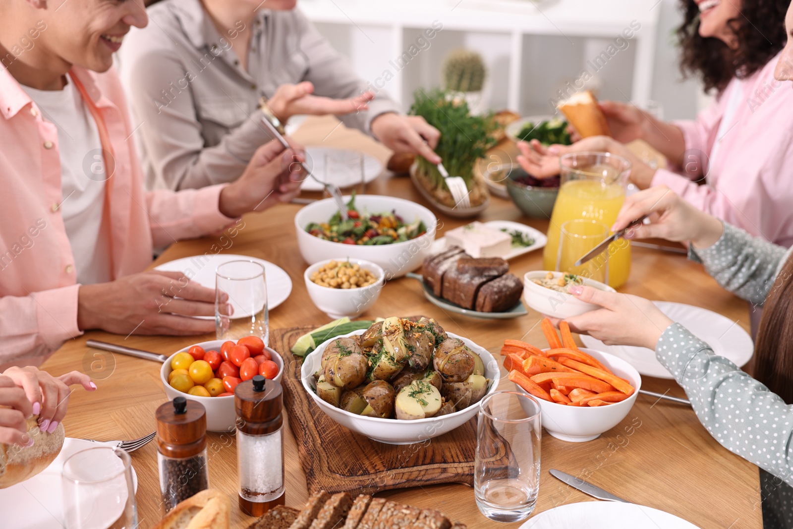 Photo of Friends eating vegetarian food at wooden table indoors, closeup