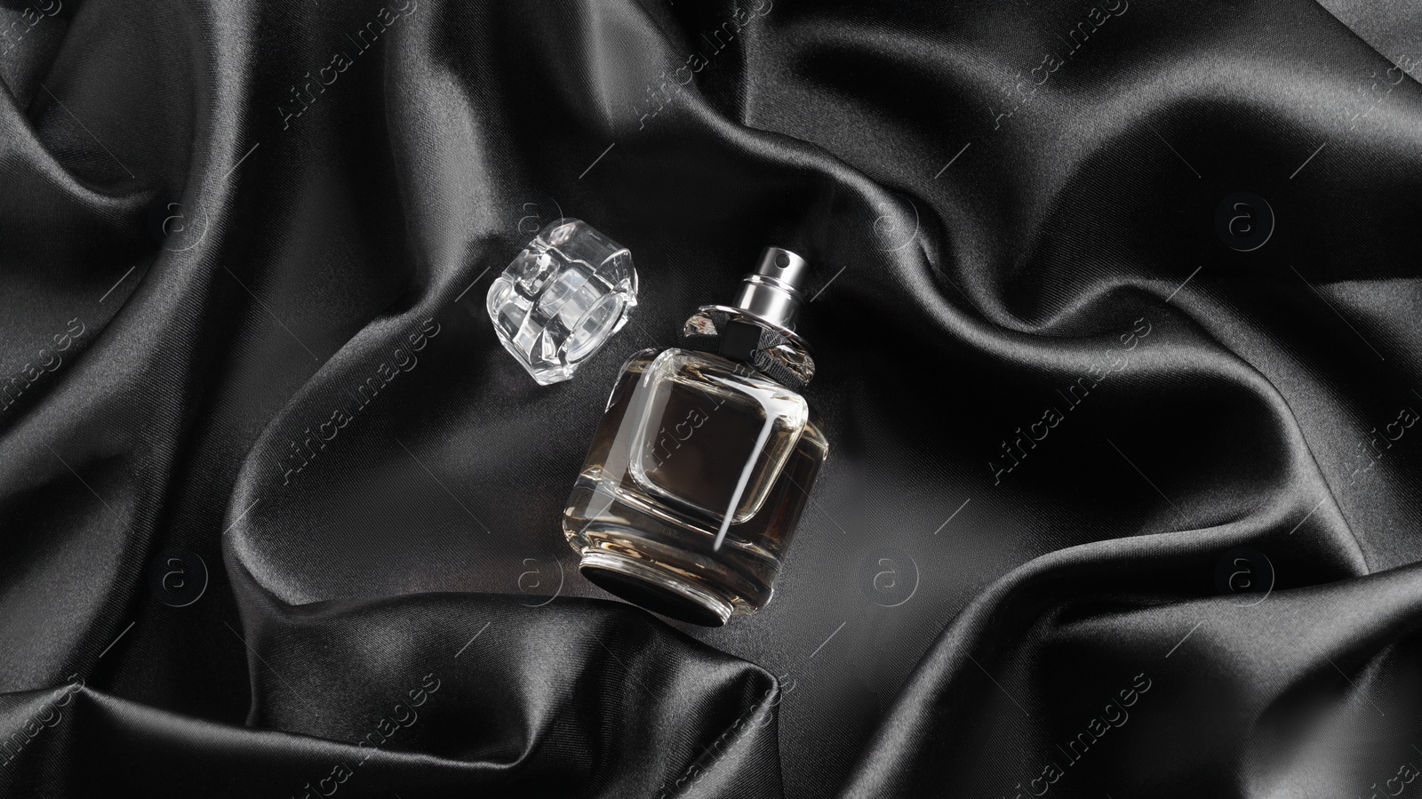 Photo of Luxury bottle of perfume on black silk, top view