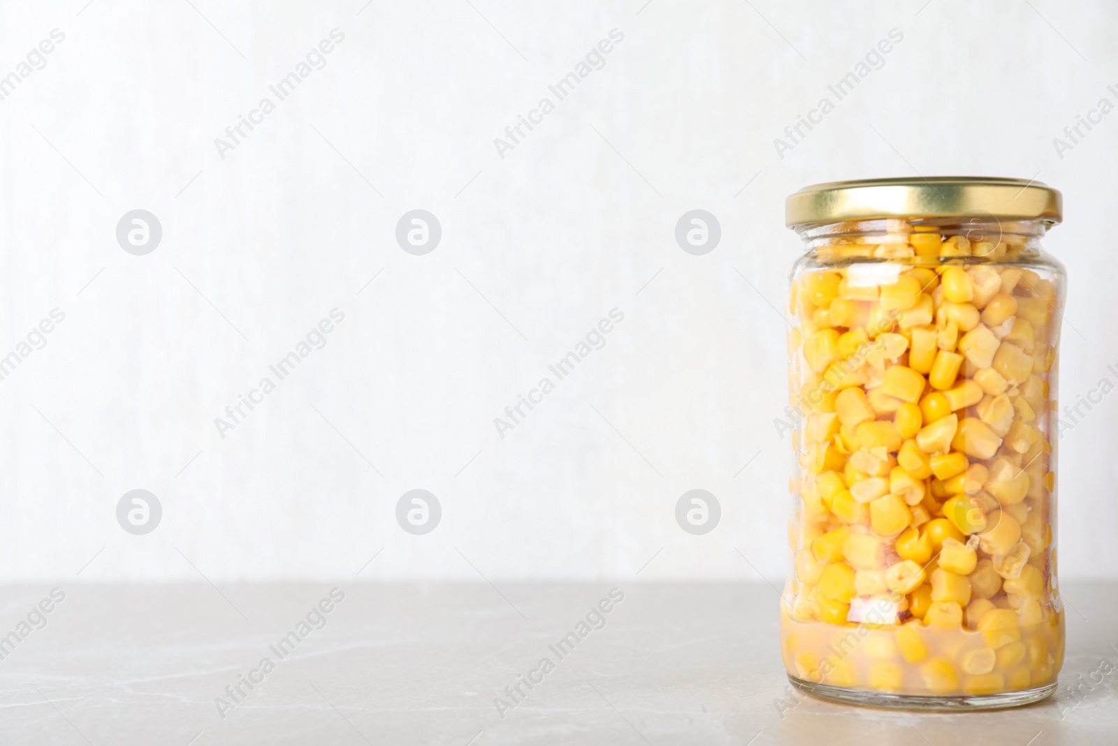 Photo of Glass jar of pickled sweet corn on light marble table. Space for text