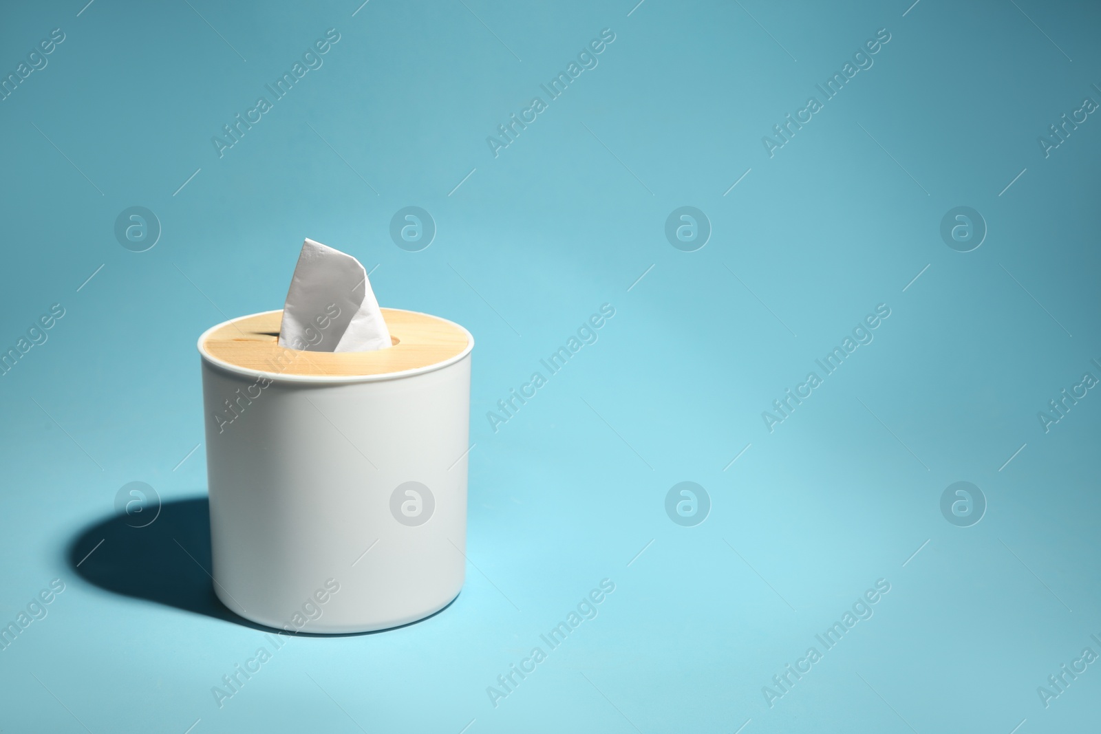 Photo of Holder with paper tissues on light blue background. Space for text