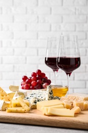 Photo of Cheese plate with honey, grapes and nuts on grey table, against brick wall