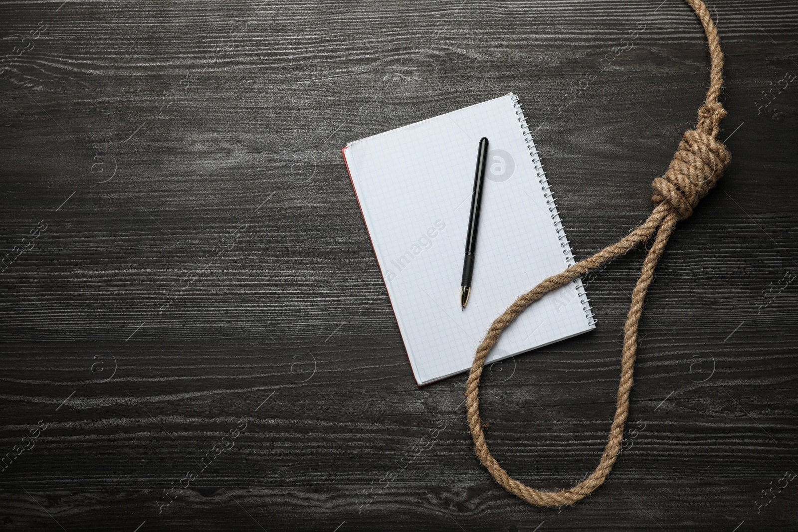 Photo of Rope noose and blank notebook with pen on black wooden table, flat lay. Space for text