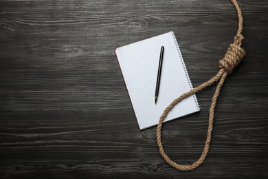 Rope noose and blank notebook with pen on black wooden table, flat lay. Space for text