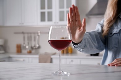 Photo of Woman refusing to drink red wine at home, closeup. Alcohol addiction treatment