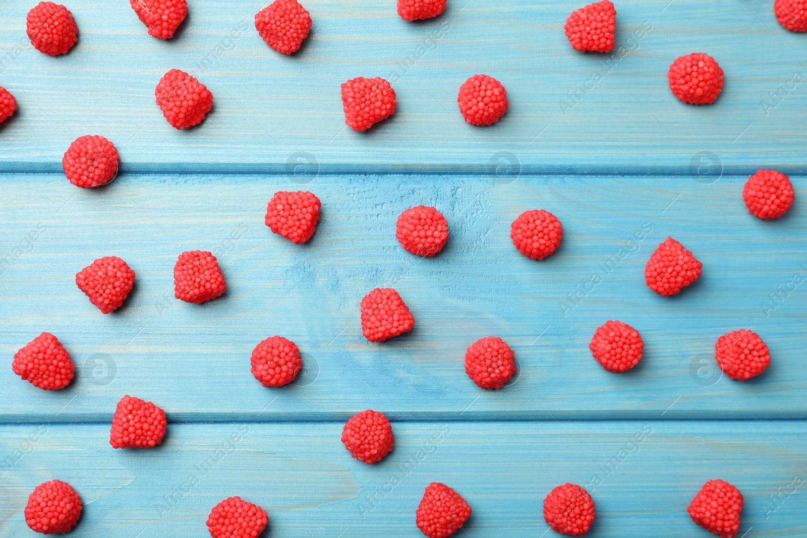 Photo of Delicious gummy raspberry candies on light blue wooden table, flat lay