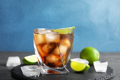 Glass of cocktail with cola, ice and cut lime on table