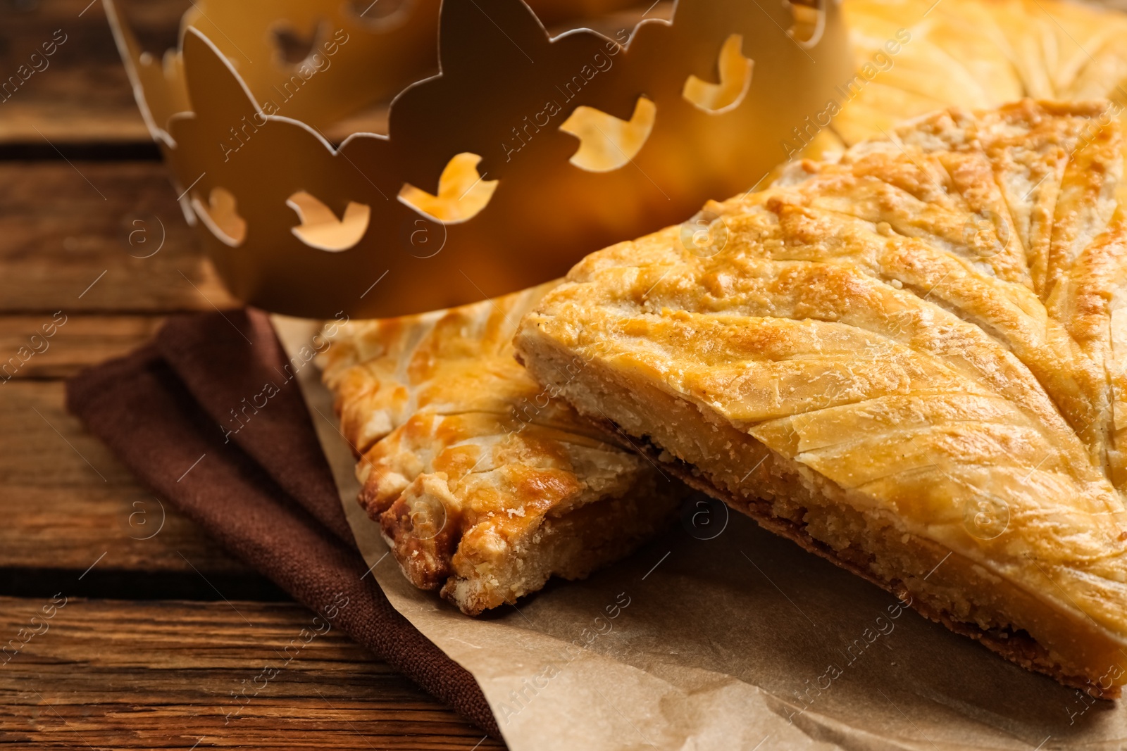 Photo of Traditional galette des Rois with paper crown on wooden table, closeup