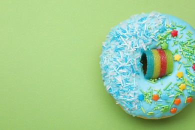 Photo of Glazed donut decorated with sprinkles on green background, top view. Space for text. Tasty confectionery