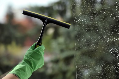 Photo of Woman cleaning glass with squeegee indoors, closeup