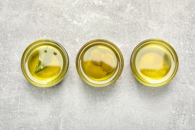 Photo of Bowls with cooking oil, olives and rosemary on light gray textured table, flat lay