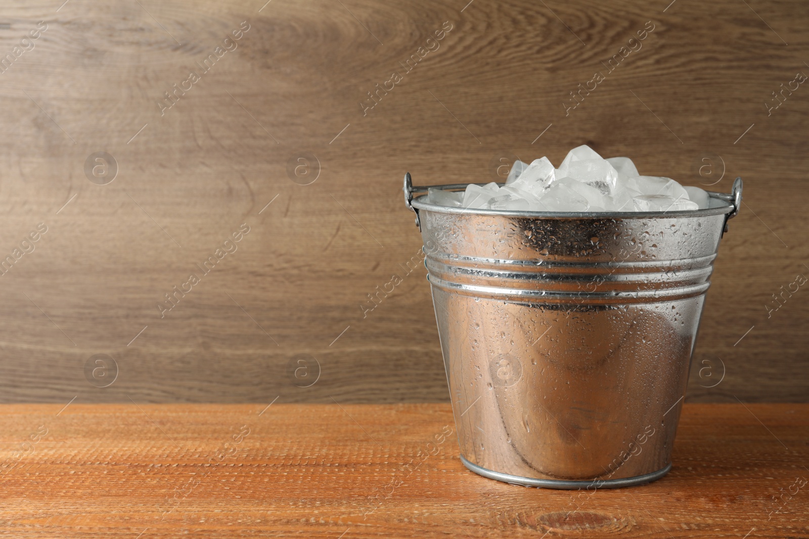 Photo of Metal bucket with ice cubes on wooden background. Space for text