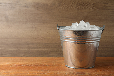 Metal bucket with ice cubes on wooden background. Space for text