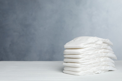 Photo of Stack of baby diapers on white wooden table against grey background. Space for text