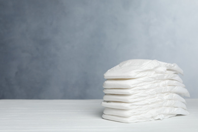 Stack of baby diapers on white wooden table against grey background. Space for text