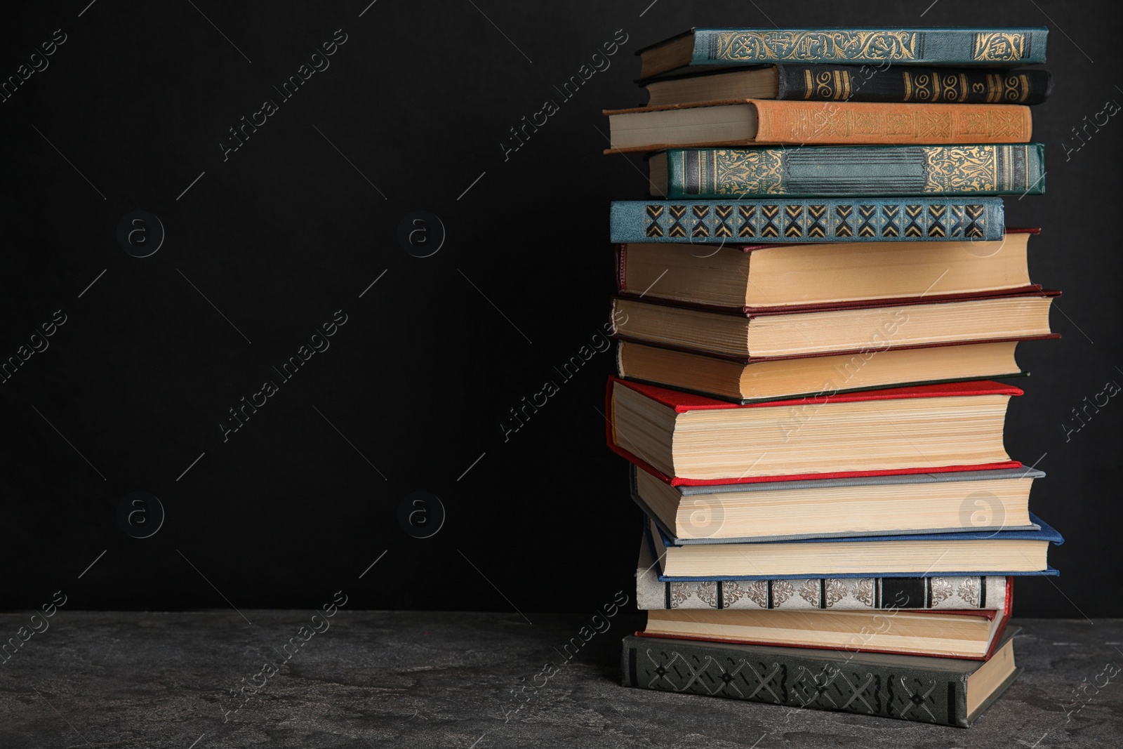 Photo of Stack of hardcover books on grey stone table against black background. Space for text