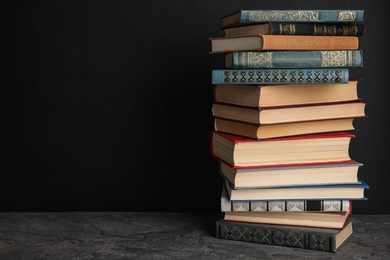 Photo of Stack of hardcover books on grey stone table against black background. Space for text