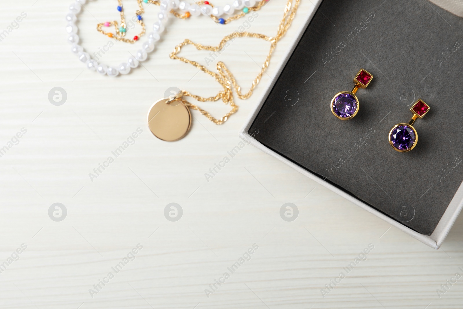 Photo of Earrings in jewel box and necklaces on white wooden table, flat lay. Space for text