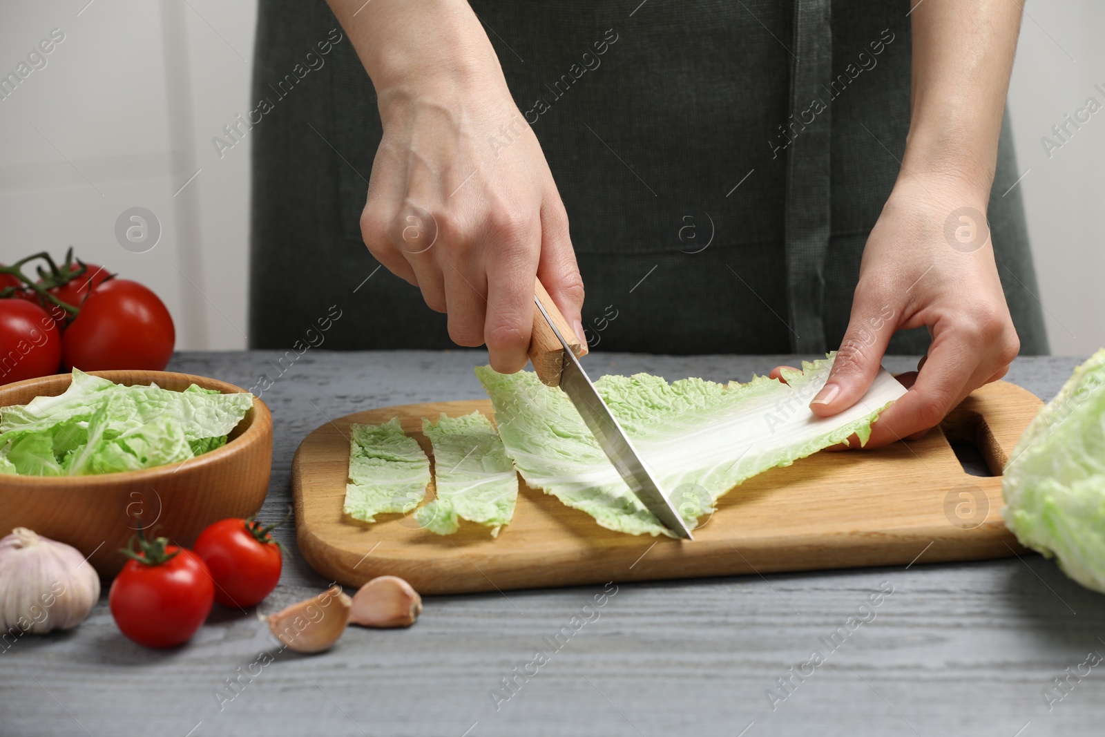 Photo of Woman cutting leaf of fresh chinese cabbage at grey wooden table in kitchen, closeup