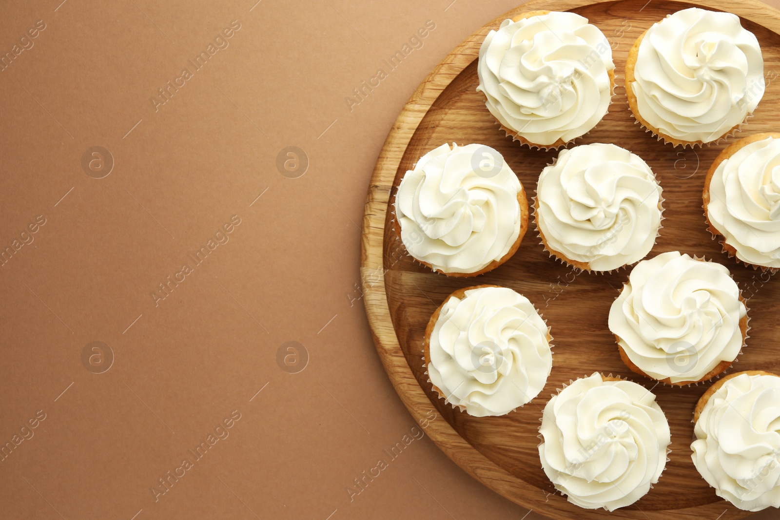 Photo of Tasty vanilla cupcakes with cream on dark beige background, top view. Space for text