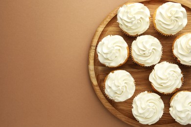 Tasty vanilla cupcakes with cream on dark beige background, top view. Space for text