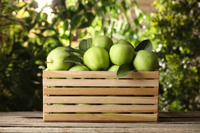 Crate full of ripe green apples and leaves on wooden table outdoors