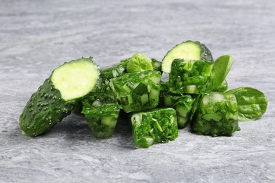 Photo of Vegetable ice cubes and fresh cucumbers on grey table