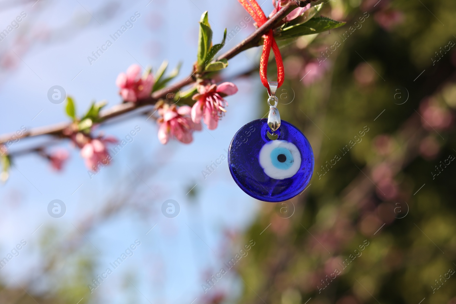 Photo of Evil eye amulet hanging on blossoming spring tree outdoors. Space for text