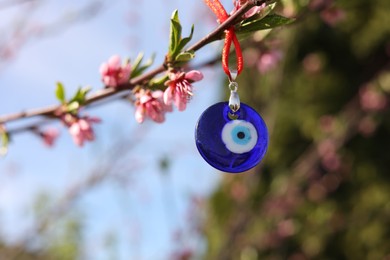 Photo of Evil eye amulet hanging on blossoming spring tree outdoors. Space for text