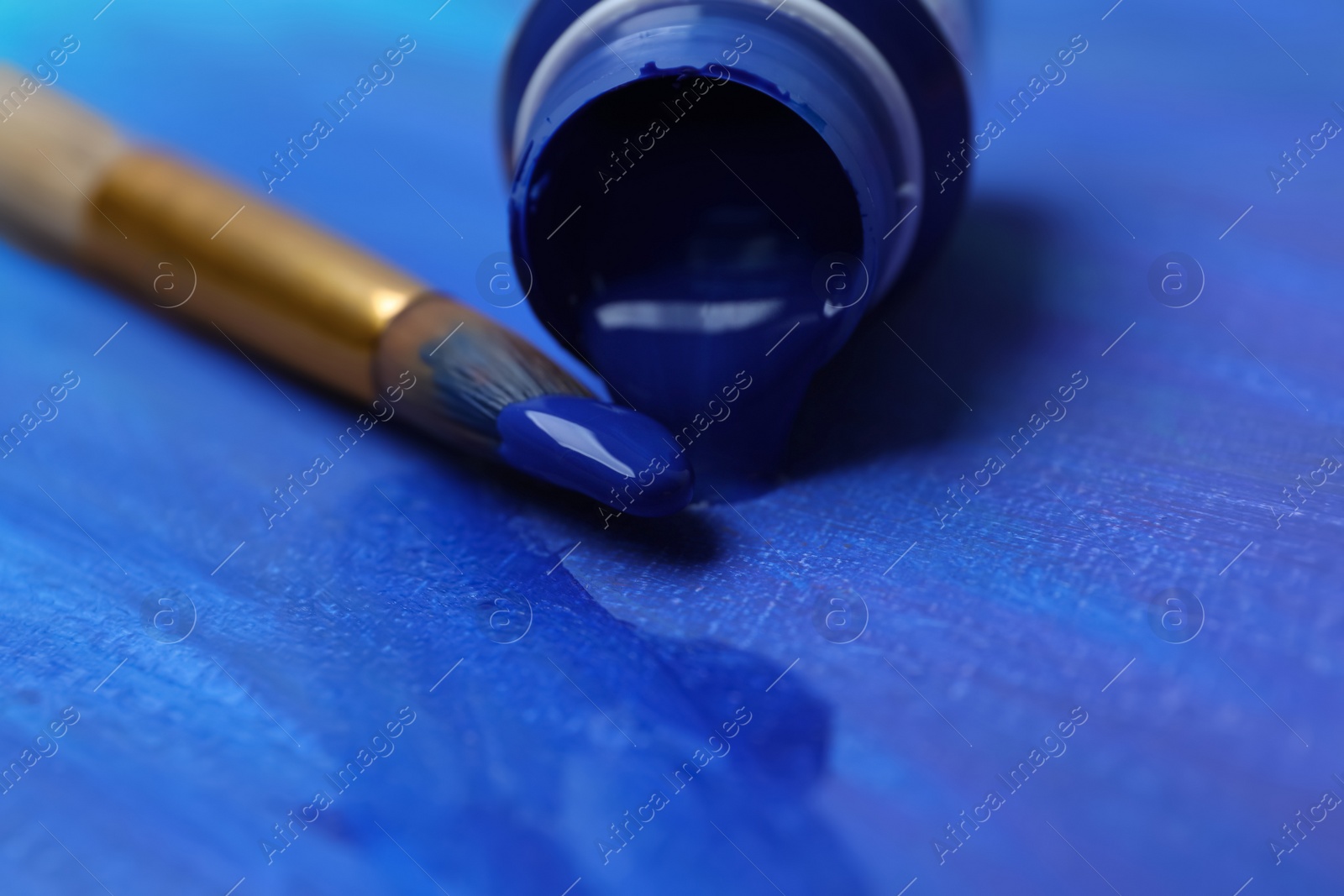 Photo of Jar with paint and brush on abstract picture, closeup