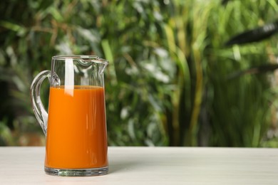 Photo of Tasty carrot juice on white table outdoors. Space for text