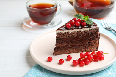 Delicious chocolate cake with red currants on white wooden table