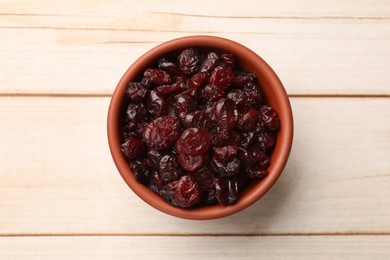 Tasty dried cranberries in bowl on light wooden table, top view