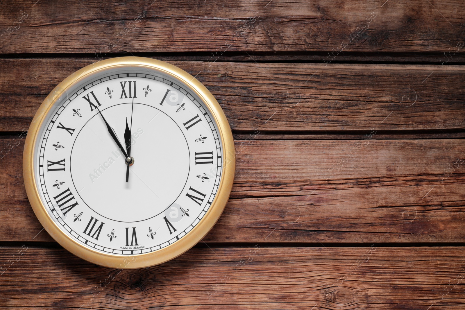 Photo of Clock showing five minutes until midnight on wooden table, top view with space for text. New Year countdown