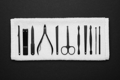 Photo of Towel with set of manicure tools on black background, top view
