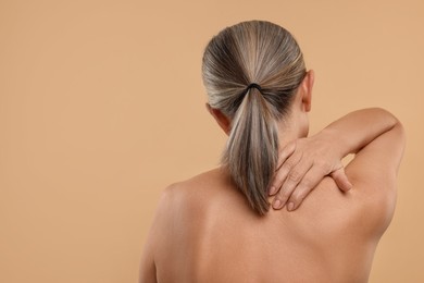 Photo of Mature woman suffering from pain in her neck on beige background, back view. Space for text