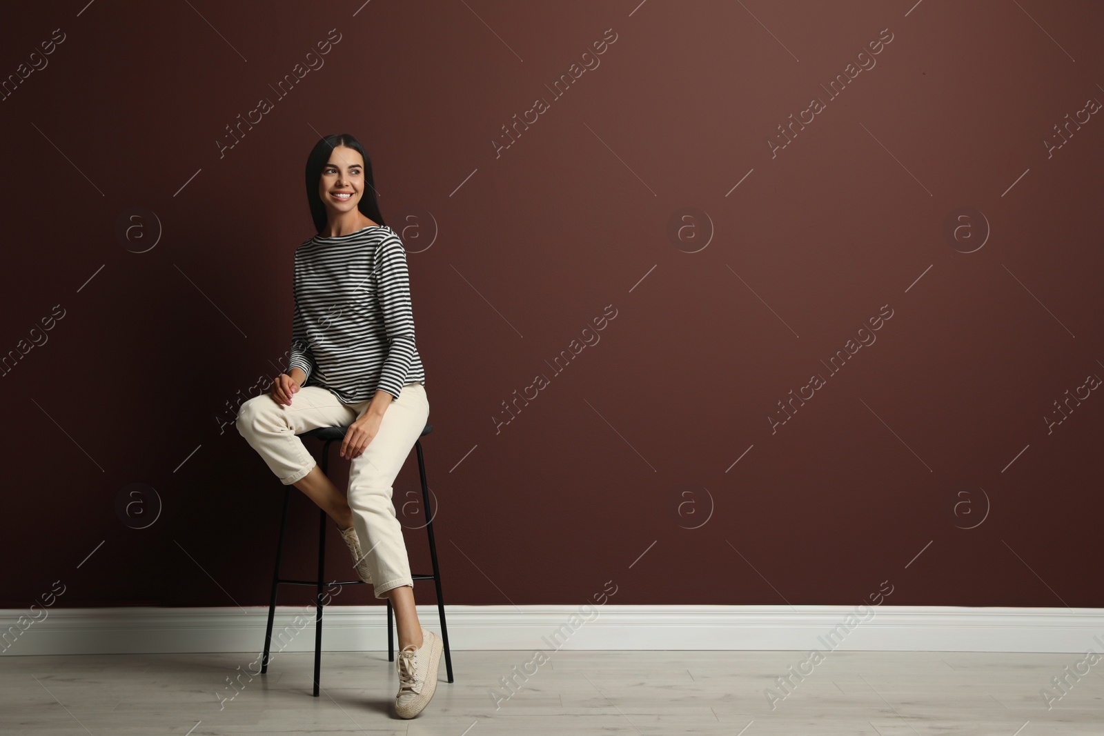 Photo of Beautiful young woman sitting on stool near brown wall. Space for text