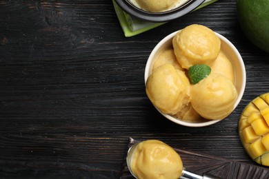 Photo of Yummy mango ice cream served on black wooden table, flat lay. Space for text