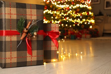 Beautiful gift boxes against fir tree with Christmas lights indoors, space for text